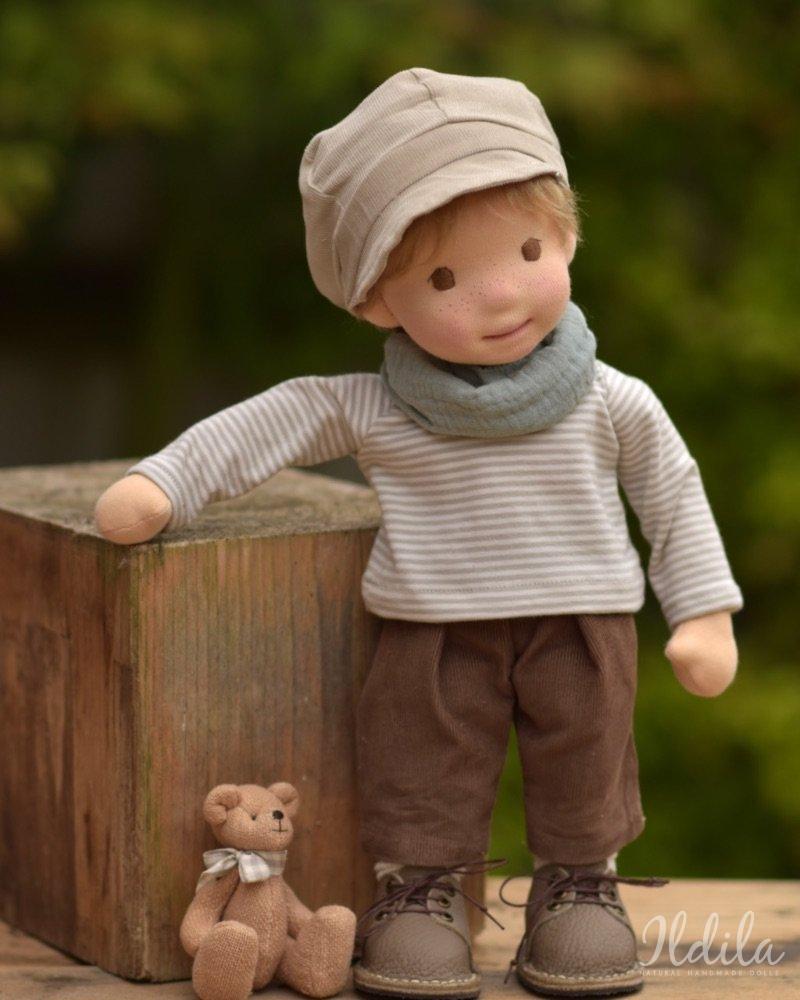 Handgemaakte stoffen pop met hoed en sjaal, staand naast een houten kist met een kleine gebreide teddybeer.