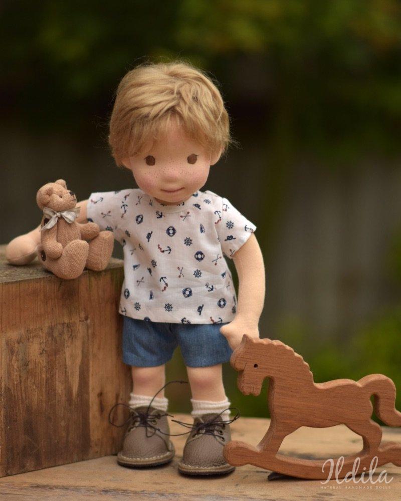 Handgemaakte pop in nautisch shirt en blauwe korte broek met een houten hobbelpaard speelgoed in haar handen.